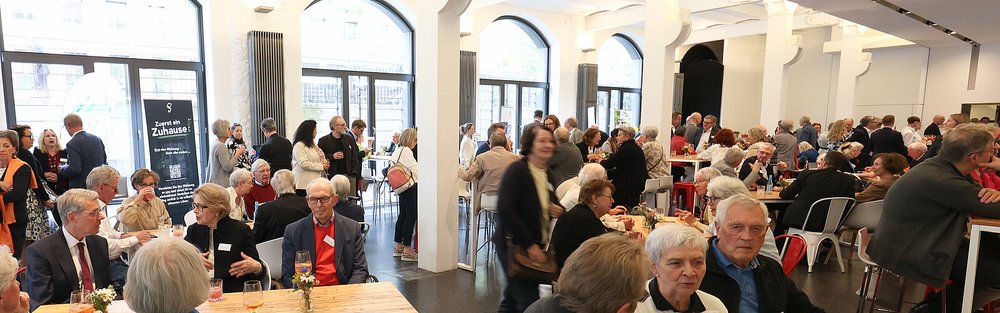 Gäste beim Empfang in einem hellen Saal mit Rundbogenfenstern – Stiftungstreffen 2024