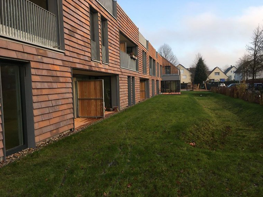 Modernes Wohnhaus mit Holzschindel-Fassade und davorliegender Rasenfläche