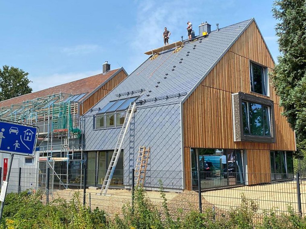 Modernes Holzhaus mit neu gedecktem Metalldach und zwei Dachdeckern auf dem First