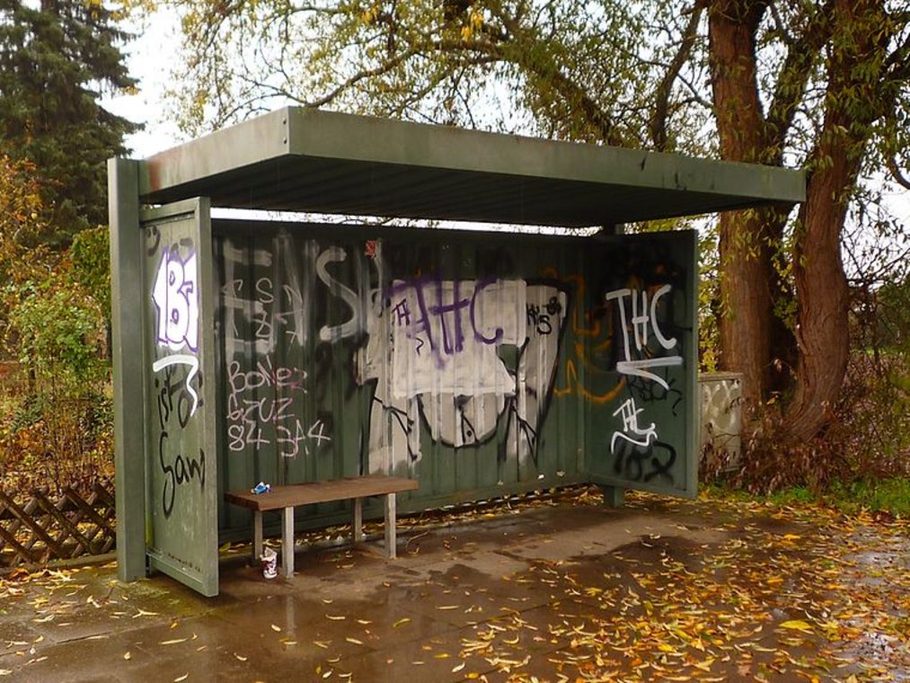 Mit Graffiti besprühte Bushaltestelle mit Bank im herbstlichen Grün