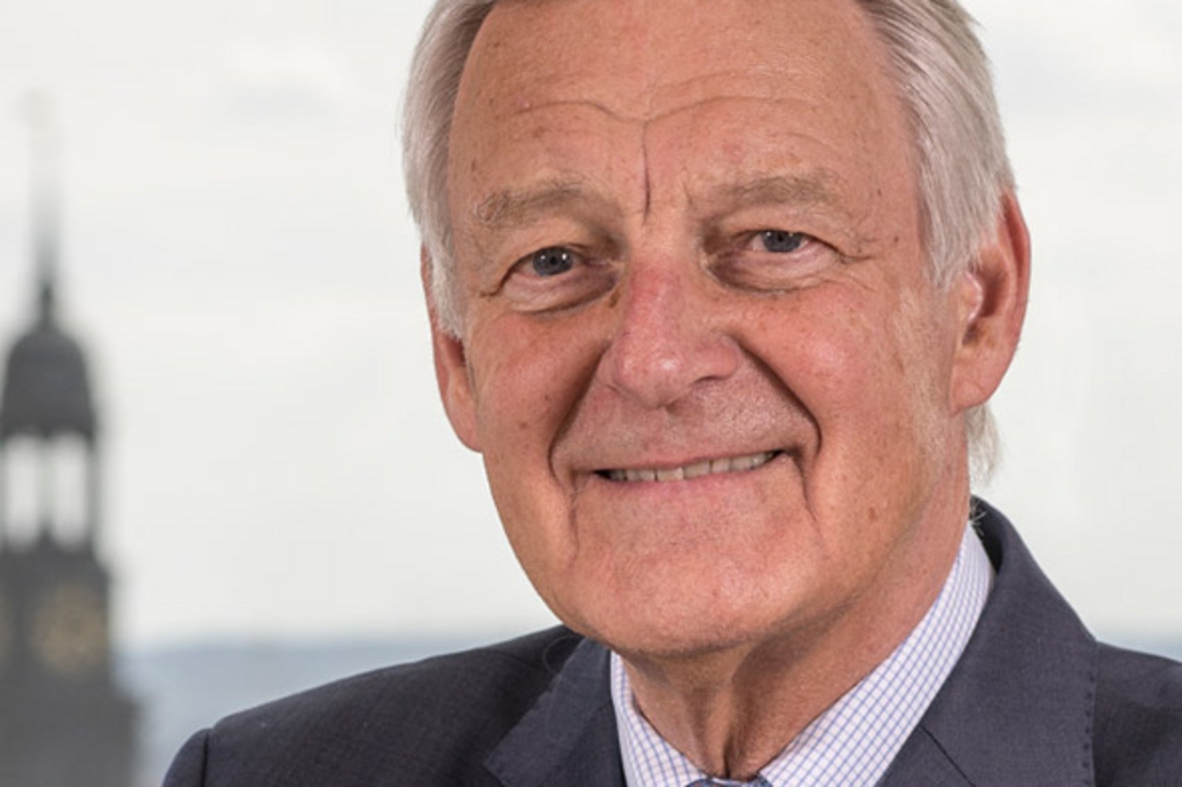 Porträtfoto von Dr. Karl-Joachim Dreyer, lächelnder Mann im Anzug vor Hamburger Kirchturm