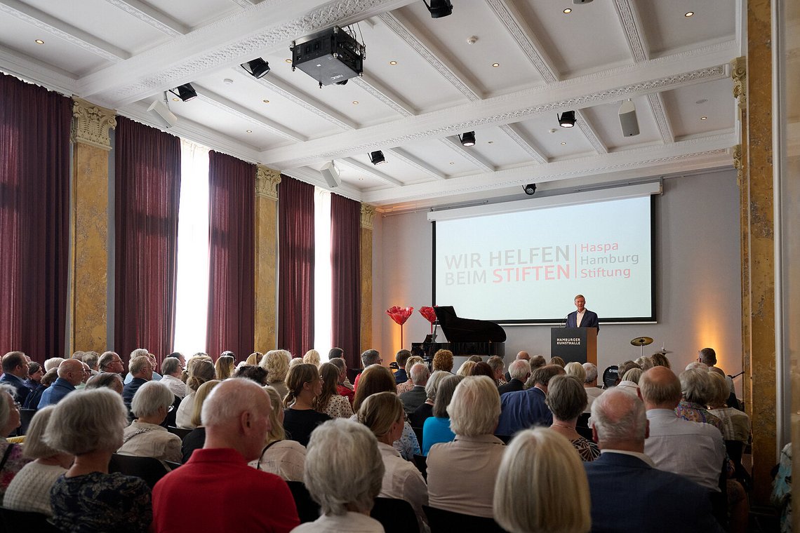 Gäste im Saal der Hamburger Kunsthalle, auf der Leinwand das Motto „Wir helfen beim Stiften“ – Stiftungstreffen 2026
