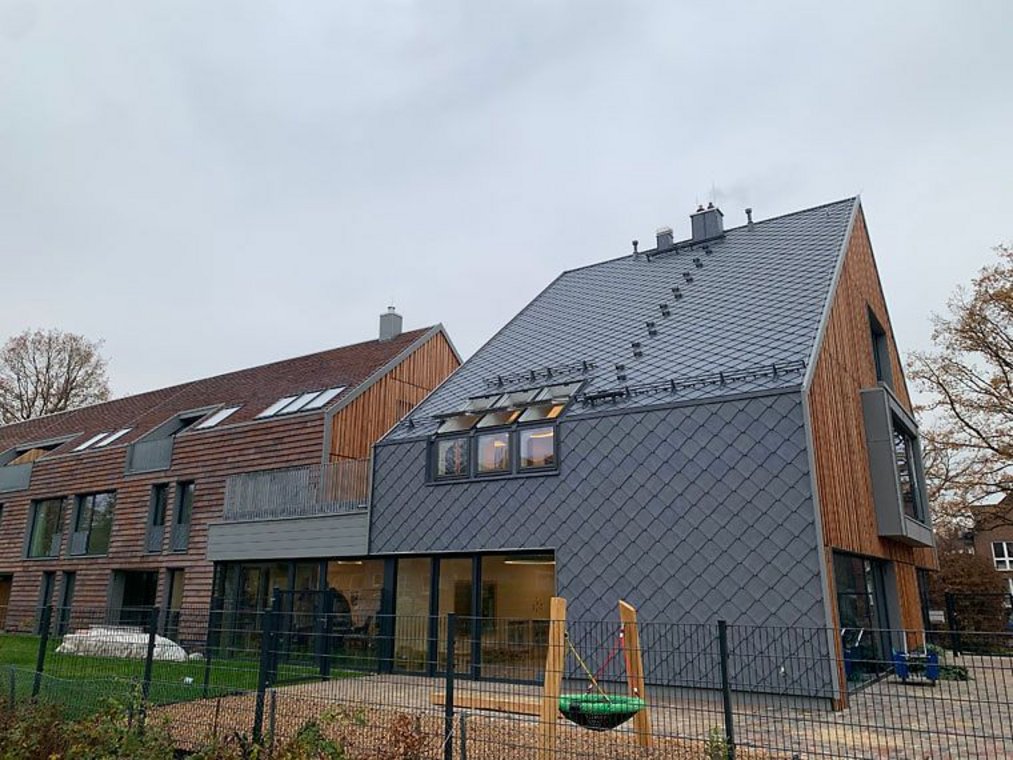 Modernes Gebäude mit grauer Schieferfassade und Spielplatz davor