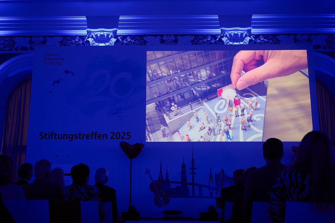Blick auf die große Leinwand mit einem Film zum Stiftungstreffen 2025 im blau beleuchteten Saal