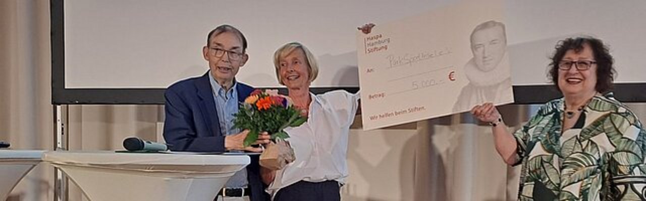 Scheckübergabe der Haspa Hamburg Stiftung an drei Personen mit Blumenstrauß
