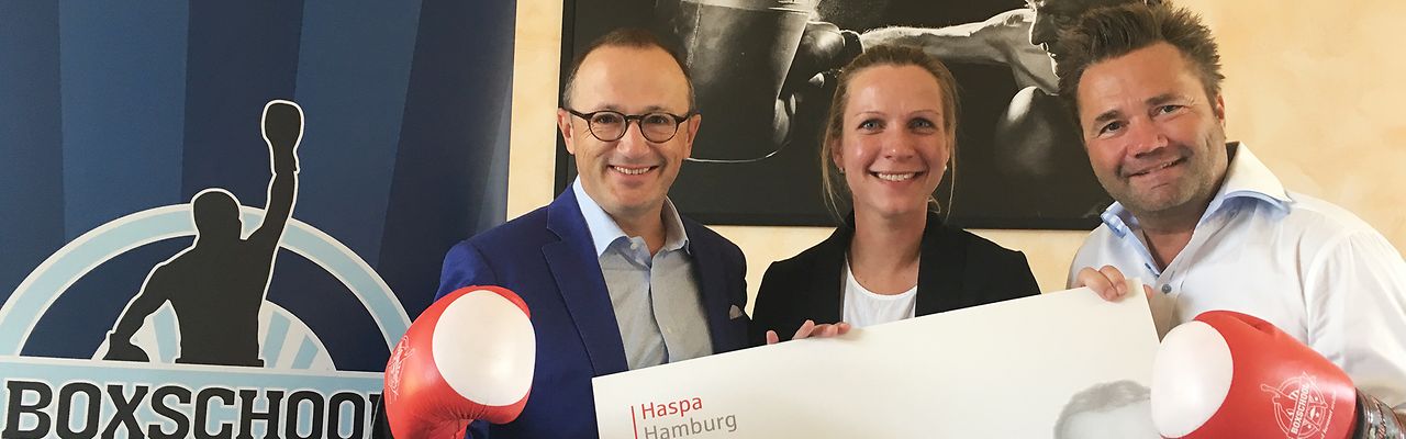 Scheckübergabe mit roten Boxhandschuhen vor dem Logo der Boxschool
