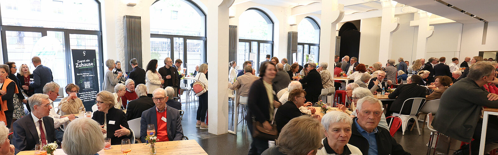 Gäste beim Empfang in einem hellen Saal mit Rundbogenfenstern – Stiftungstreffen 2024